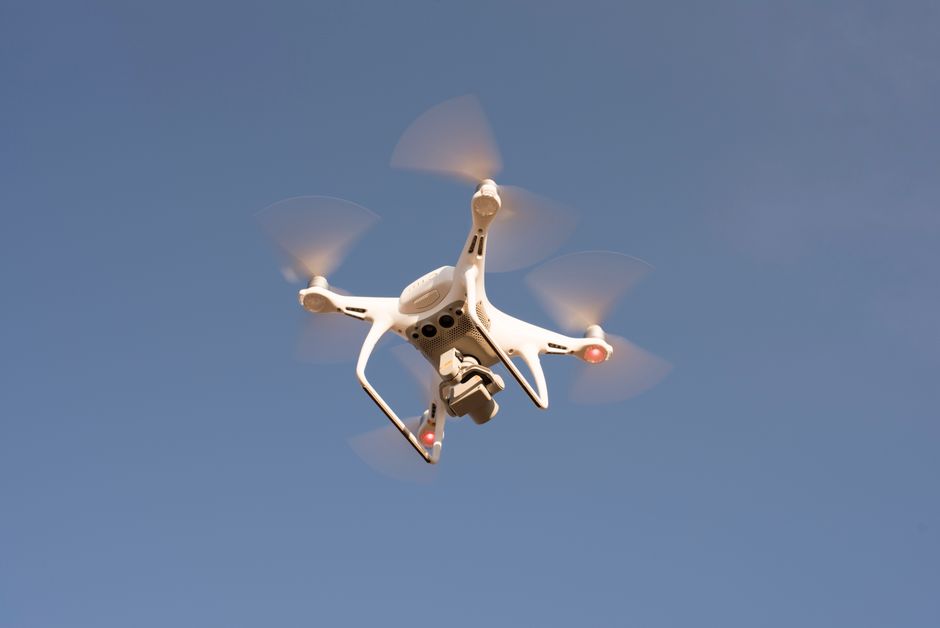 Inteligência Artificial — A white drone in flight against a clear blue sky, capturing aerial footage with precision.