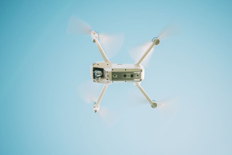 Inteligência Artificial — A sleek white drone flying under a clear blue sky, capturing aerial views.