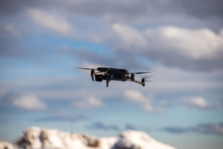 Inteligência Artificial — Aerial view of a drone flying over snow-covered mountains with dramatic clouds.